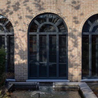 Buitenaanzicht van huis met grote toogramen en donkere maatwerk shutters