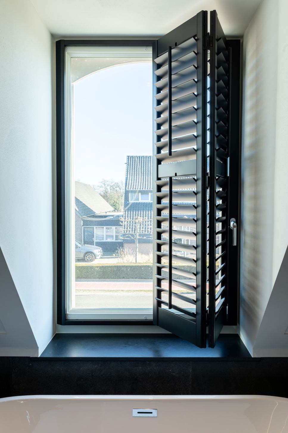 Zwarte shutters in dakkapel half opzij geschoven.